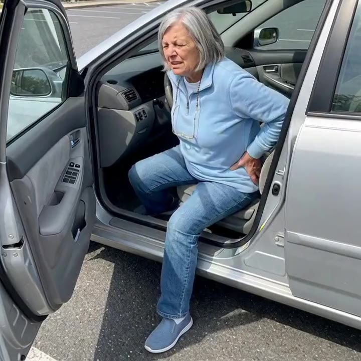 Woman in her 60s stuck in her car seat with the door open, pressing the back of her hip